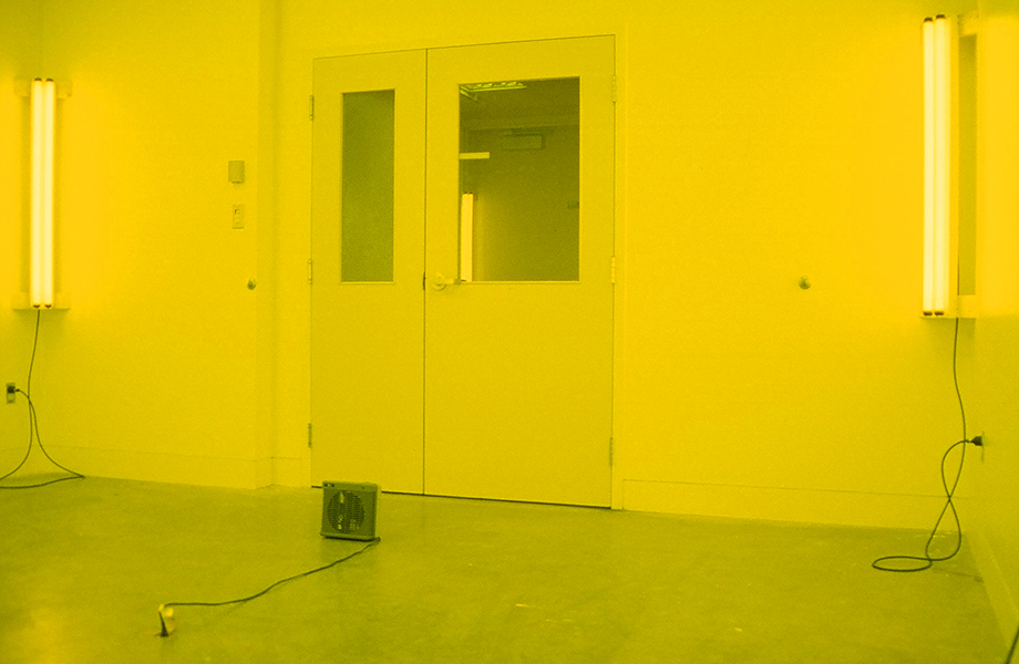 Yellow room image from TOO MUCH IN THE SUN by Kennedy Telford. The lighting in a room is covered in yellow gels and the room is heated to a warm temperature.