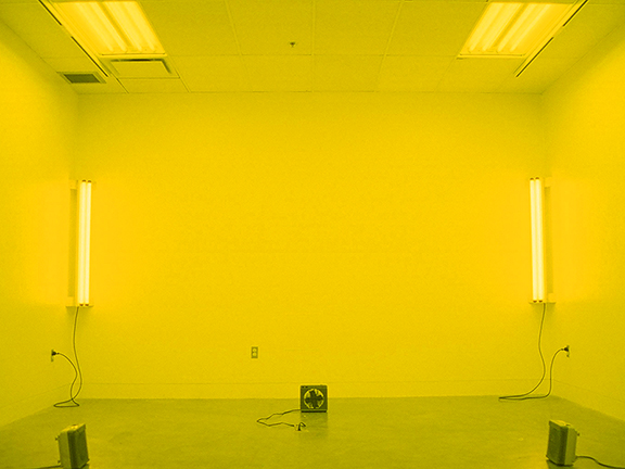 Yellow room image from TOO MUCH IN THE SUN by Kennedy Telford. The lighting in a room is covered in yellow gels and the room is heated to a warm temperature.